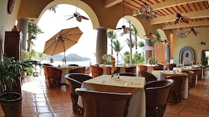 Un restaurante con terraza, mesas con manteles blancos y ventiladores de techo.