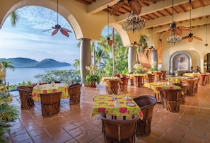 Un restaurante con terraza, mesas con manteles florales y vista al mar.
