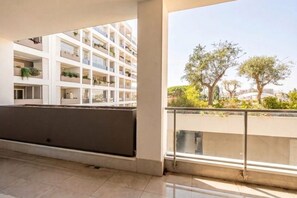 Un edificio moderno con diversi balconi, alcuni con piante, e una vista aperta su alberi e un panorama urbano lontano.