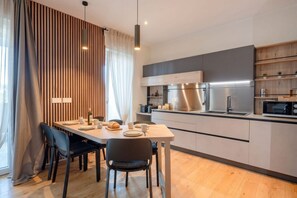 Una cucina moderna con zona pranzo, caratterizzata da una parete in legno, elettrodomestici in acciaio inossidabile e pavimento in legno chiaro.