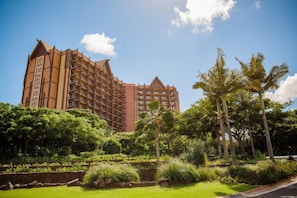 Un hôtel à plusieurs étages, de style architectural traditionnel, entouré d’une végétation luxuriante et de palmiers.