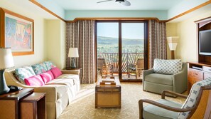 Ein Hotelzimmer mit Sofa, Sessel und kleinem Tisch. Ein Balkon bietet Blick auf die Landschaft.