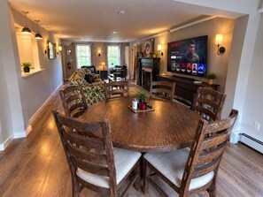 A dining area with a round wooden table surrounded by chairs, a television mounted on the wall, and a fireplace. - Wiley Inn | Cozy King Room with Bathtub (Peru)