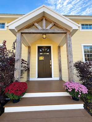 A house with a front porch, a brown door, and two flower pots with red and pink flowers. - The Wiley | Stylish Queen Room Near Ski Bar (Peru)