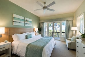 Habitación de hotel con cama, escritorio, silla, cómoda, ventilador de techo y vista al exterior.