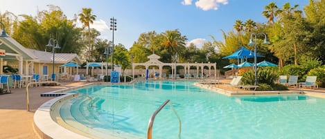 Une piscine dotée d’un parasol, de chaises longues et d’un kiosque.