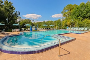 Une piscine dont le bord est recouvert de carrelage, entourée de chaises longues et de parasols.