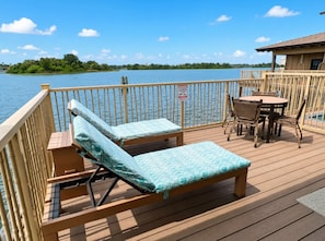 Eine Holzterrasse mit Liegestühlen und einem Tisch mit Blick auf ein Gewässer.