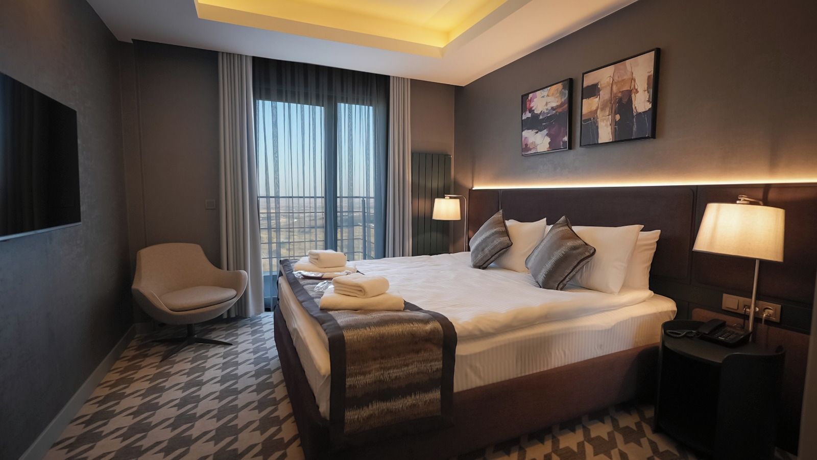 Una habitación de hotel con una cama grande, una silla, un escritorio con lámpara y una ventana con cortinas.