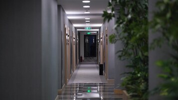 Pasillo de hotel con un camino despejado hacia la salida, un extintor y una planta a la derecha.