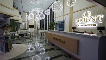 Zona de recepción de hotel con diseño moderno, que incluye mostrador de recepción, área de estar e iluminación decorativa.