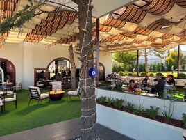 Un espacio exterior para comer con mesas y sillas, un árbol y vistas a la calle.