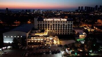 Un hotel con un letrero llamativo, un estacionamiento y una vista del paisaje urbano al fondo.