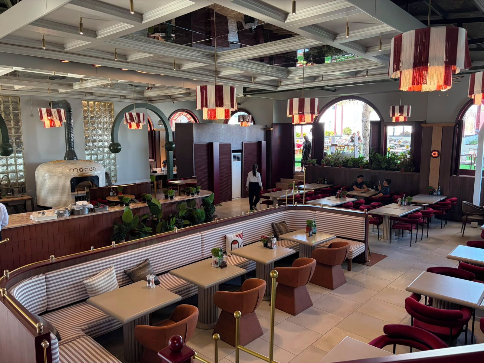 L’intérieur d’un restaurant, avec un espace central aménagé pour les clients, des tables et un four à pizza.