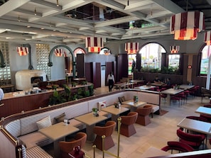 A restaurant interior with a central seating area, tables, and a pizza oven. - Lorent Hotel İncek (Ankara)