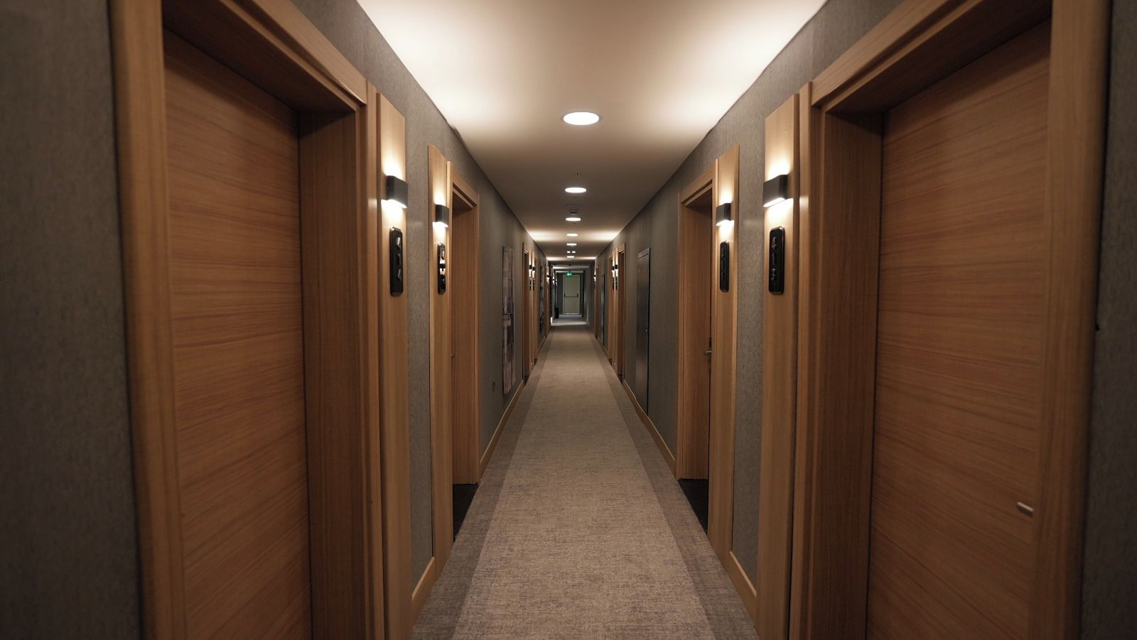 Un pasillo de hotel con puertas de madera, suelo alfombrado e iluminación empotrada.