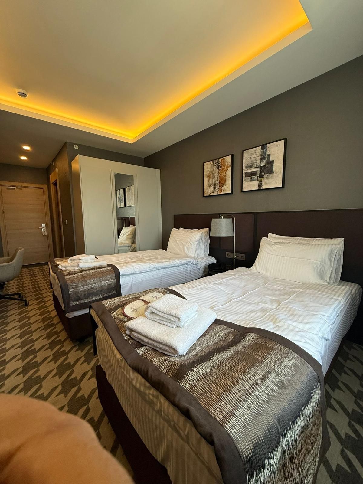 Una habitación de hotel con dos camas, un escritorio, una silla y obras de arte en la pared.