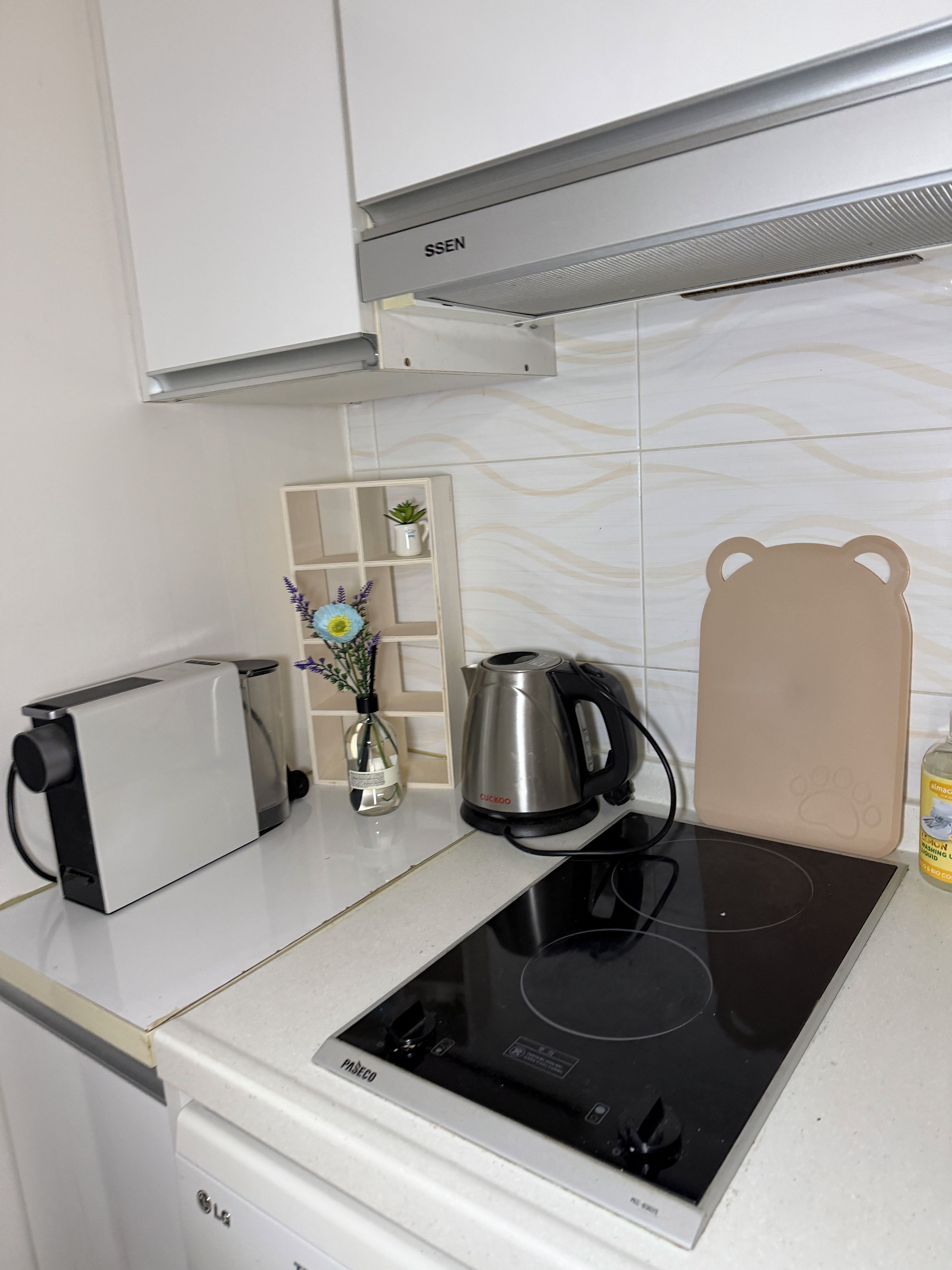Une cuisine équipée d’une plaque de cuisson à induction intégrée, d’un grille-pain, d’une bouilloire et d’un meuble de rangement au-dessus.