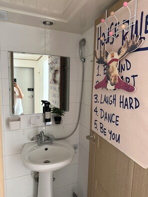 Ett badrum med handfat, spegel och en motiverande affisch på väggen.