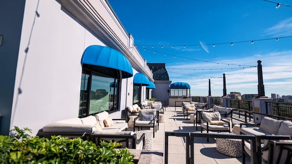 A rooftop terrace with outdoor seating, a view of the cityscape, and string lights. - Orlando | Cozy Riviera Retreat | Pool + Resort (Lake Buena Vista)