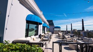 Una terraza en la azotea con mobiliario exterior, vistas de la ciudad y luces colgantes.