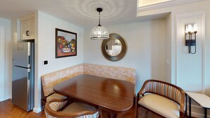 Un comedor con una mesa de madera, dos sillas, un refrigerador, un espejo decorativo y una lámpara colgante.