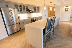 Une cuisine moderne dotée d’appareils électroménagers en acier inoxydable, d’un îlot central avec un plan de travail en marbre et de luminaires suspendus.