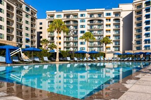 Un espace piscine d’hôtel avec de nombreux chaises longues et parasols, entouré de grands immeubles.