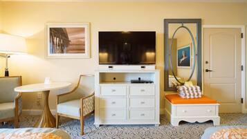 A hotel room with a television, a desk, a chair, a bedside table, and a bed.