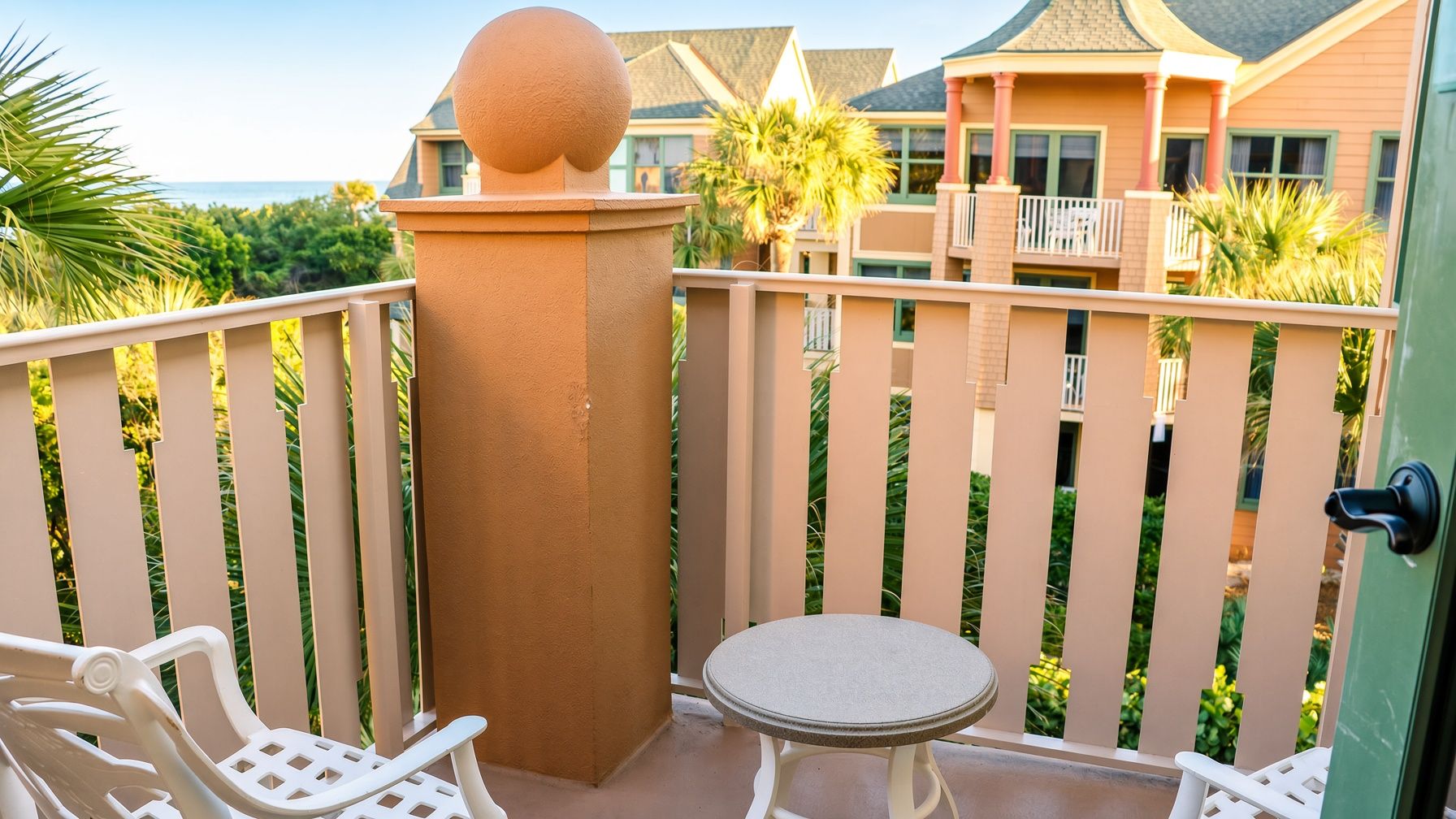 A balcony with a round table and two chairs, a decorative column, and a view of a building with a balcony.