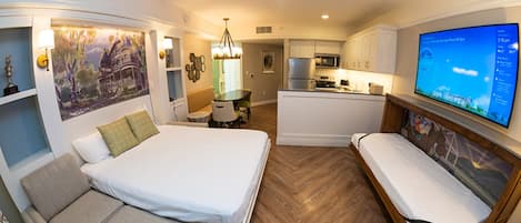 Quarto de hotel com cama, sofá, televisão, ventoinha no teto e cozinha.