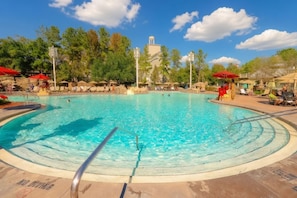 A large outdoor swimming pool with clear blue water, surrounded by lounge chairs and umbrellas, and a backdrop of trees and a building. - Orlando | Romantic Park Retreat | Pool + Spa (Lake Buena Vista)