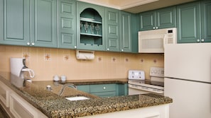 Eine Küche mit türkis-blauen Schränken, einem weißen Kühlschrank, einer Mikrowelle, einem Herd, einer Kaffeemaschine und einem Toaster.