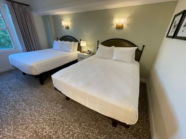 Een hotelkamer met twee eenpersoonsbedden, een nachtkastje met een lamp en een raam met gordijnen.