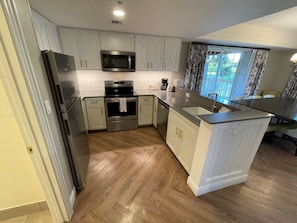 Une cuisine avec des meubles blancs, des appareils en acier inoxydable et un parquet en bois disposé en motif chevrons.