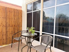 Une terrasse avec une table ronde et deux chaises, une clôture en bambou et une grande fenêtre.