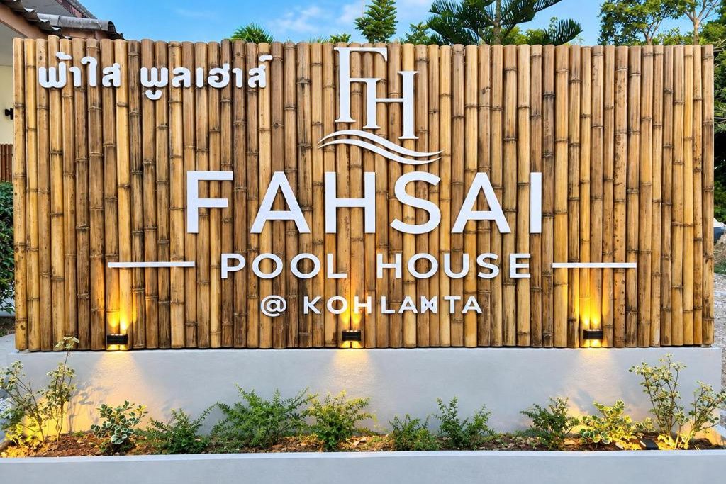 A sign for FAHSAI POOL HOUSE at KOHLANTA with a bamboo backdrop and illuminated letters.