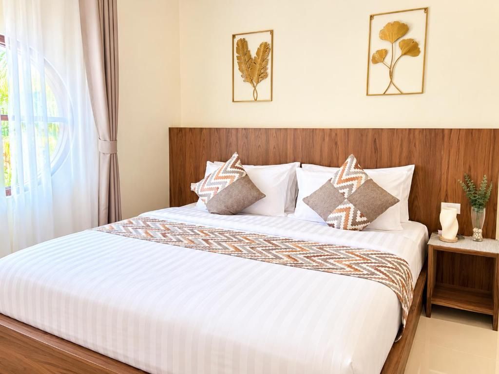 A hotel room with a large bed, a wooden headboard, and two wall-mounted leaf artwork.