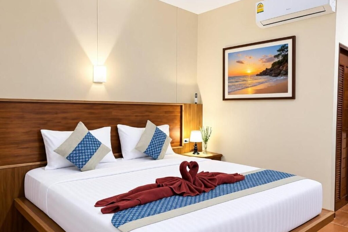 Une chambre d’hôtel avec un lit, des oreillers, une table de chevet, une lampe, un tableau encadré au mur et une serviette sur le lit.