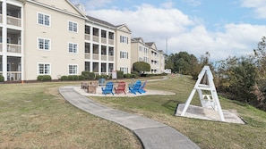 A multi-story building with a landscaped lawn, outdoor seating area, and a white structure resembling a ladder. - Myrtle Beach | Laid-Back Waterway Break | Pool + Lazy River | 2BR (Myrtle Beach)