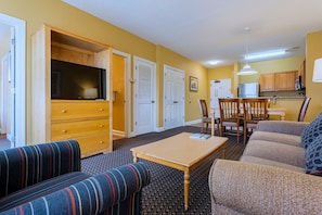 A living room with a sofa, a coffee table, a TV, and a kitchen area in the background. - Myrtle Beach | Laid-Back Waterway Break | Pool + Lazy River | 2BR (Myrtle Beach)