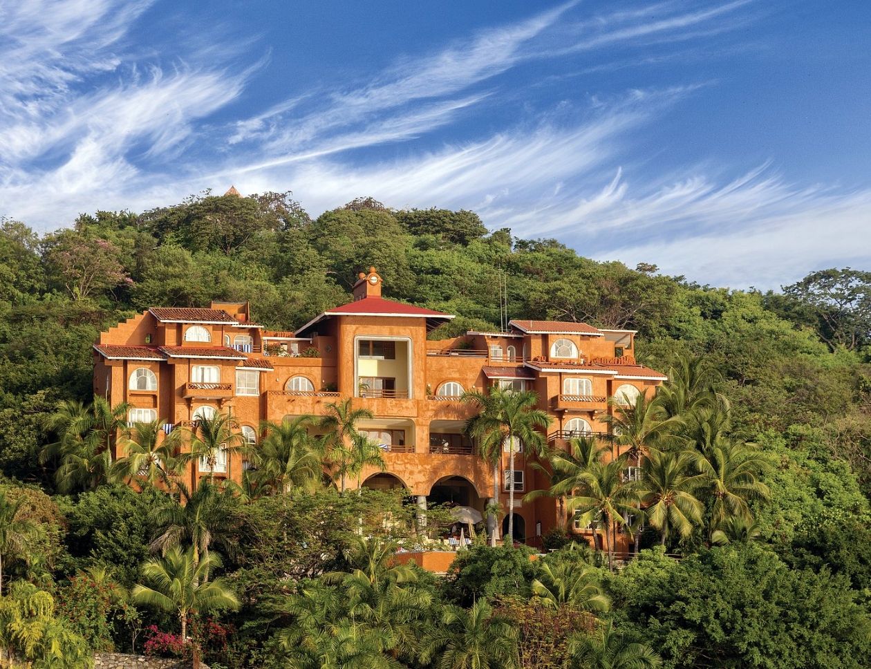 A large, multi-story building with a central courtyard, surrounded by dense tropical vegetation.