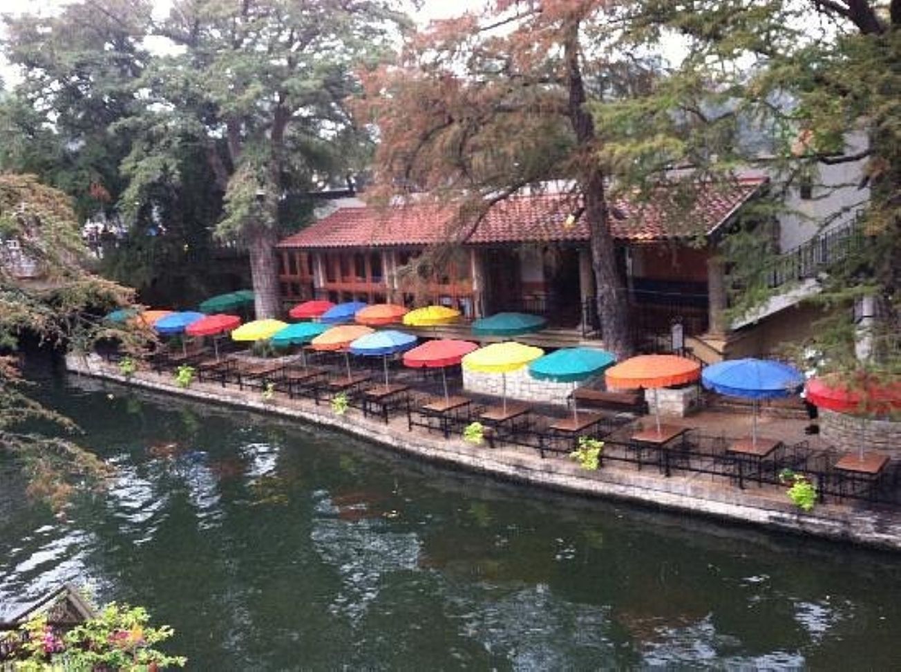 Um restaurante à beira do rio, com mesas ao ar livre e guarda-sóis coloridos.