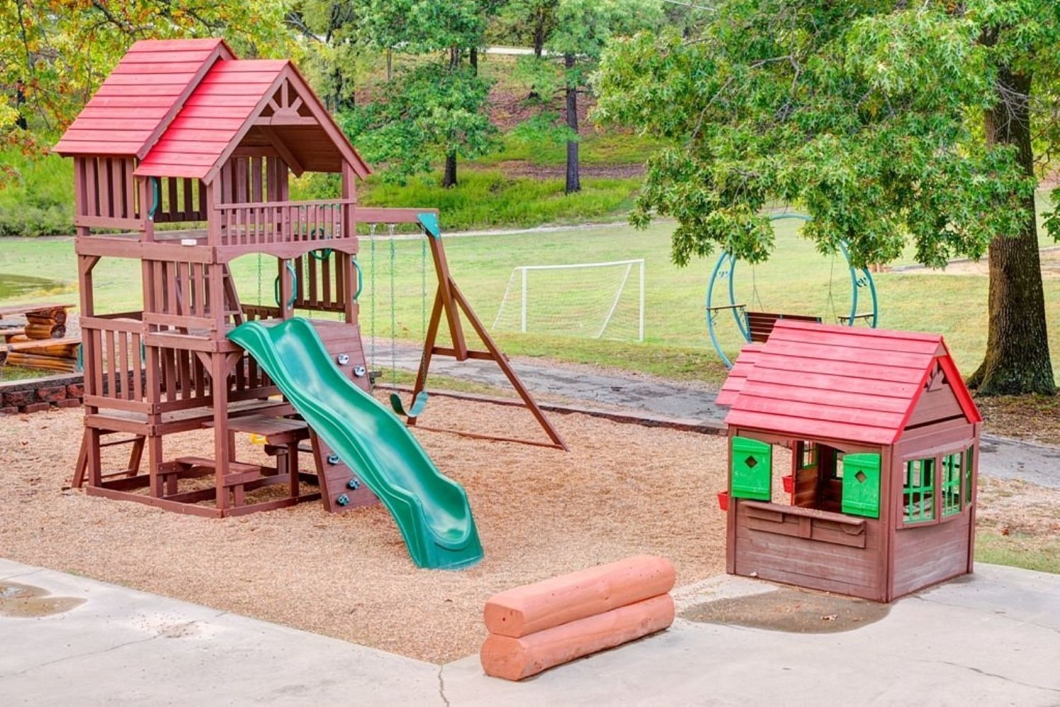 Un parque infantil con una casita de madera, un tobogán y columpios.