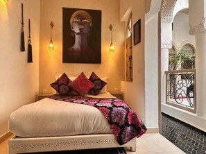 A bedroom with a bed, pillows, a blanket, a painting, and a balcony with a railing. - Riad Dollar des Sables & Spa (Marrakech)