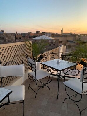 A rooftop terrace with a table and chairs, a view of the city skyline, and a decorative fence. - Riad Dollar des Sables & Spa (Marrakech)