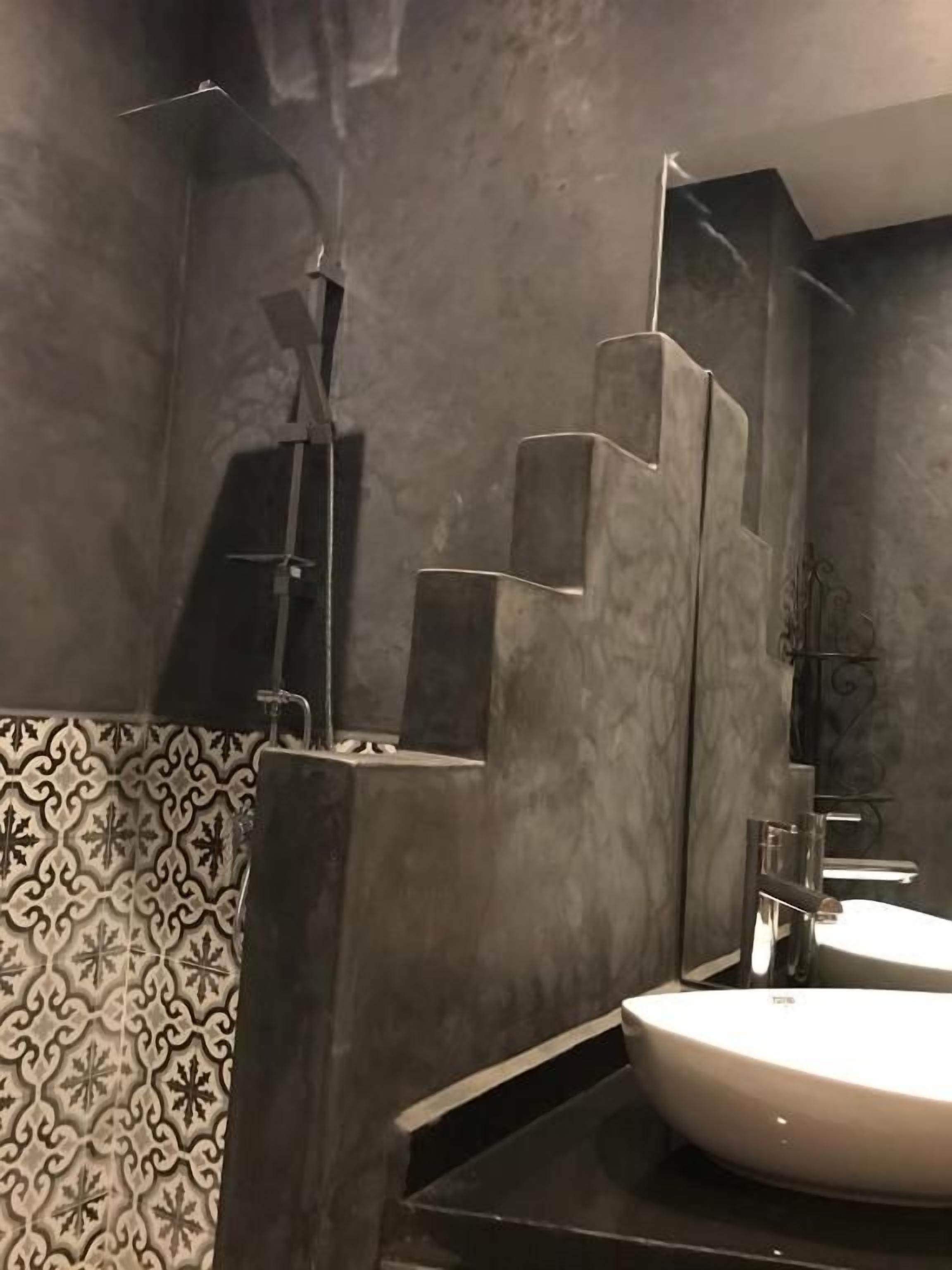 A bathroom with a modern design, featuring a large sink, a shower area, and a patterned wall.