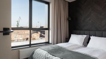 Ein modernes Schlafzimmer mit großem Fenster, einem Bett mit gesteppter Bettdecke und einem Kopfende mit Fischgrätmuster.