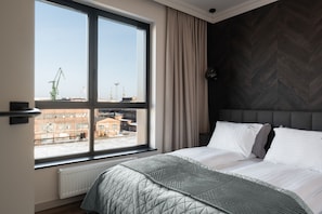 Ein modernes Schlafzimmer mit großem Fenster, einem Bett mit gesteppter Bettdecke und einem Kopfende mit Fischgrätmuster.