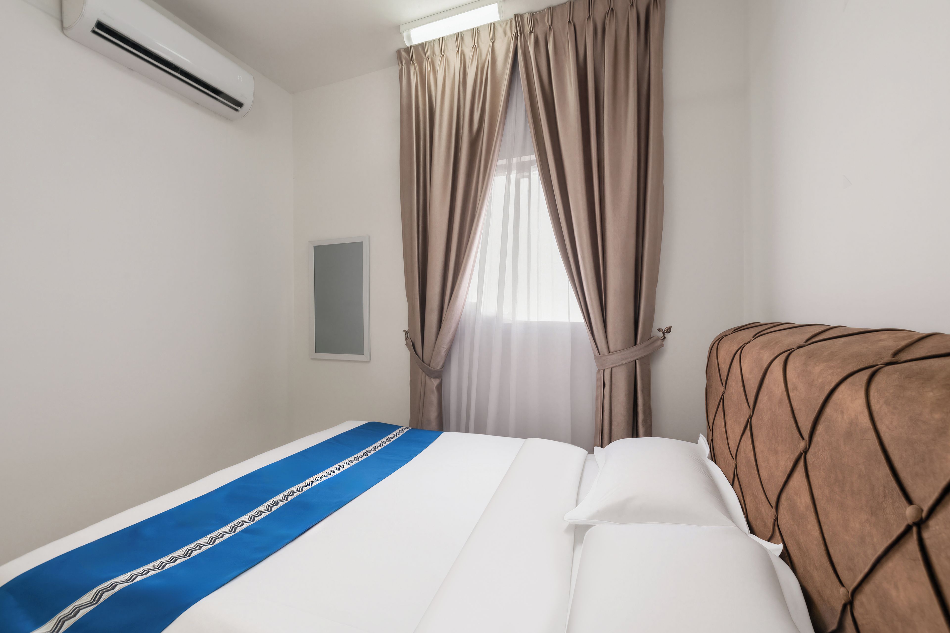 Habitació d'hotel amb llit, finestra amb cortines, aire condicionat i televisió penjada a la paret.